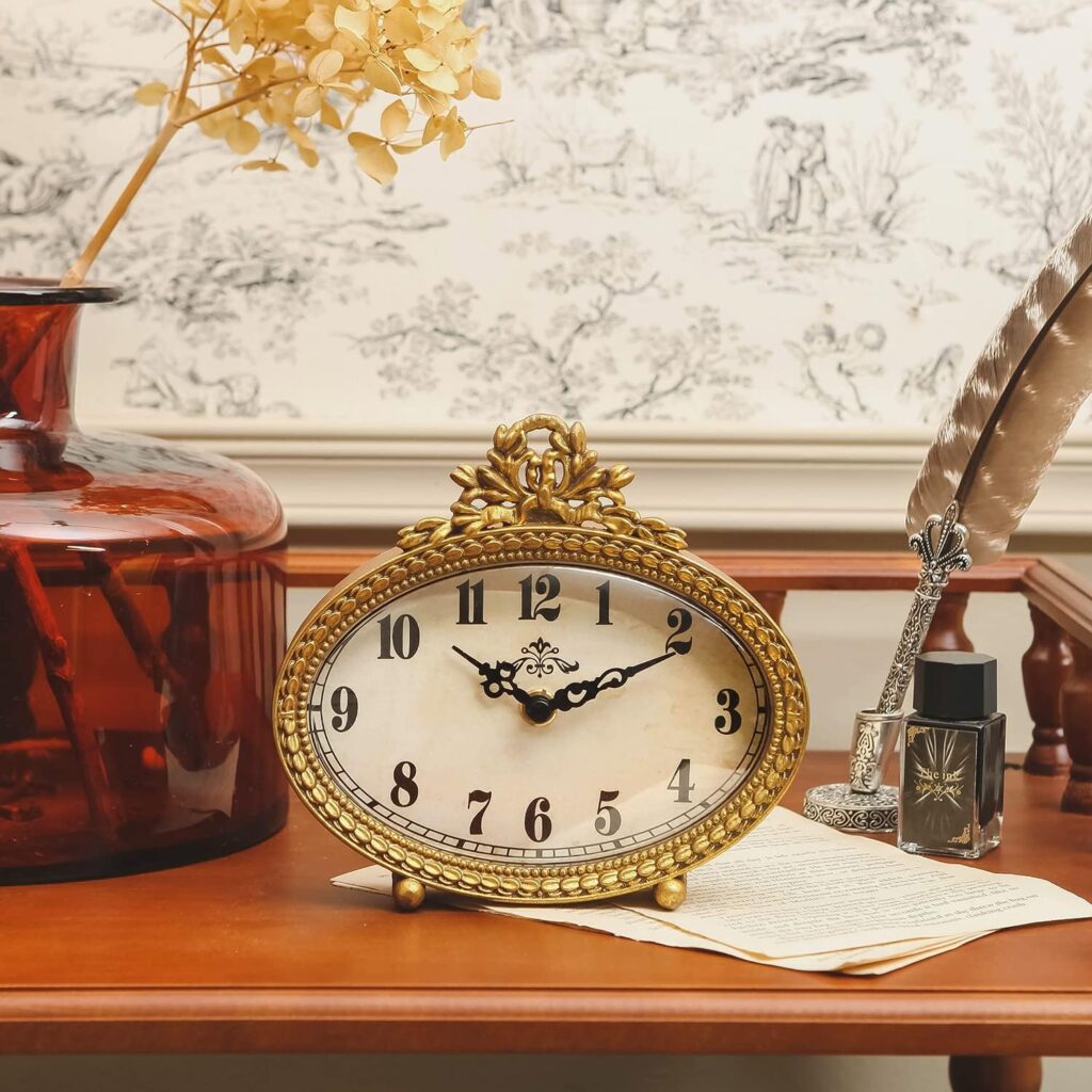 Gold vintage oval tabletop clock with ornate floral detailing, antique-style face, and black hand. Styled for French cottage or Victorian inspired decor