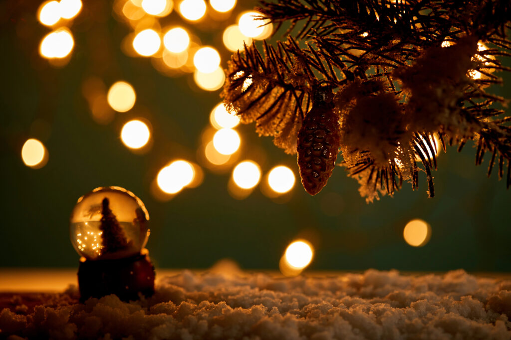 Moody Christmas Decor with warm golden lights, evergreen branches, pinecones, and a small snow globe on a cozy winter surface